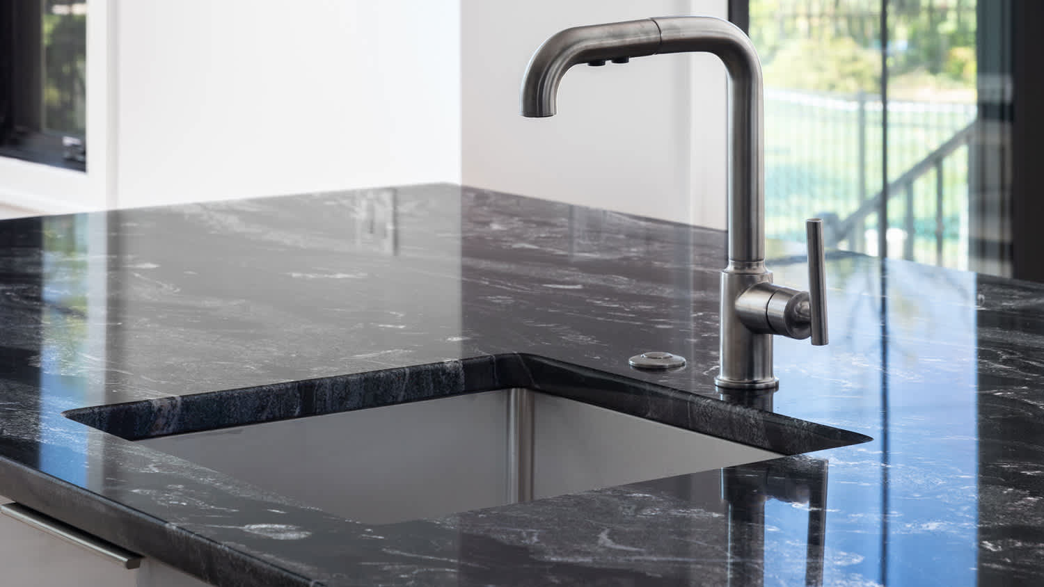 A stainless kitchen faucet detail on a black marble countertop