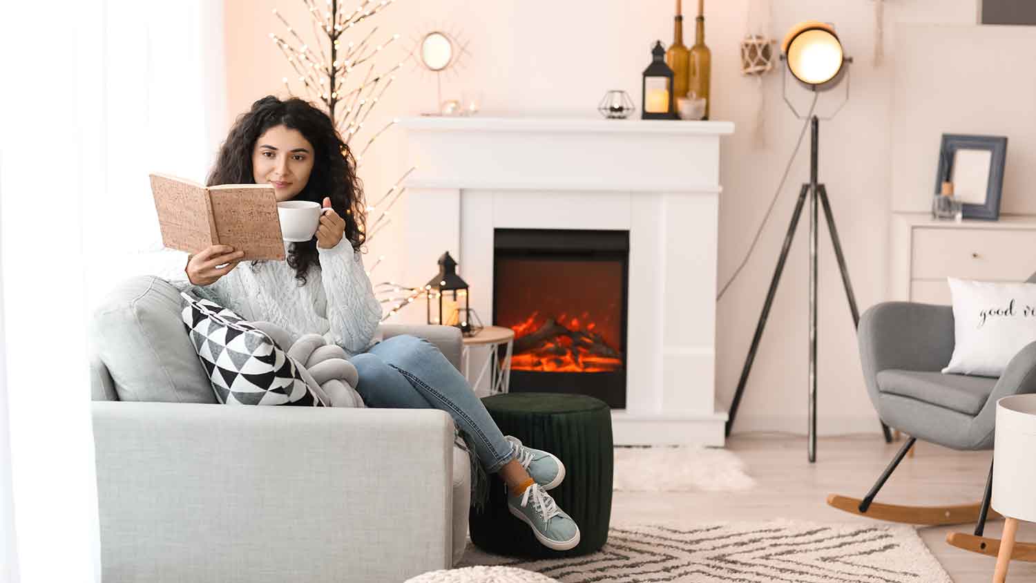Woman sitting on a couch and reading a book near the fireplace