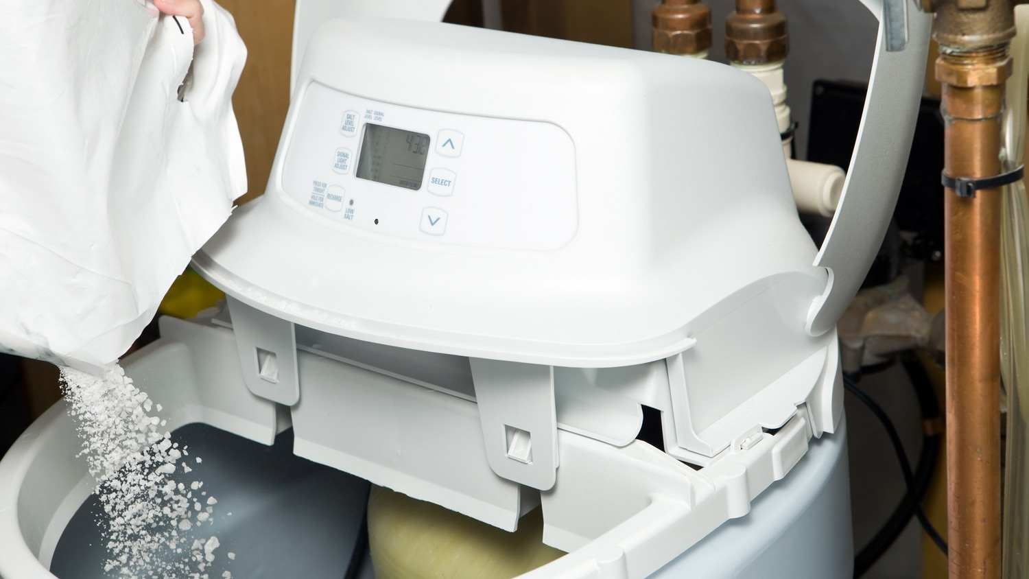None A hand filling water softener’s tank with salt