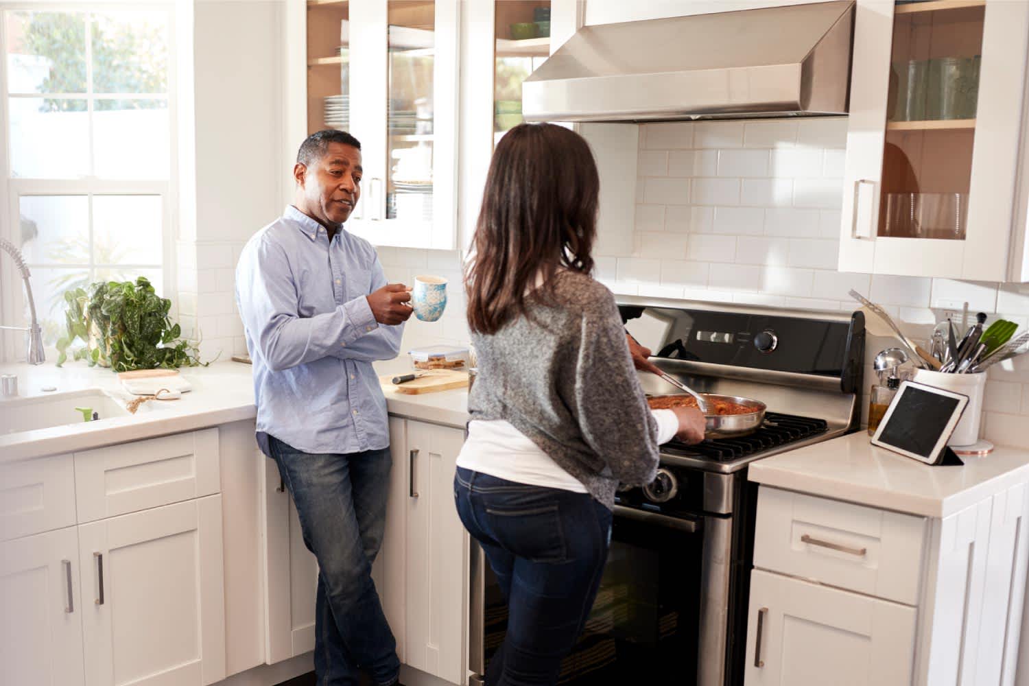 None A couple cooking some food over stove in the kitchen