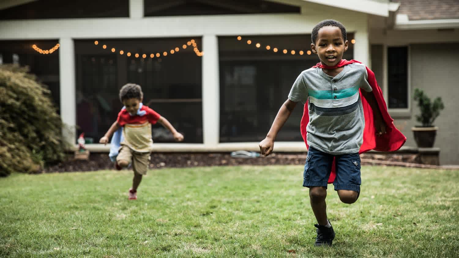 Boys in capes running in the backyard