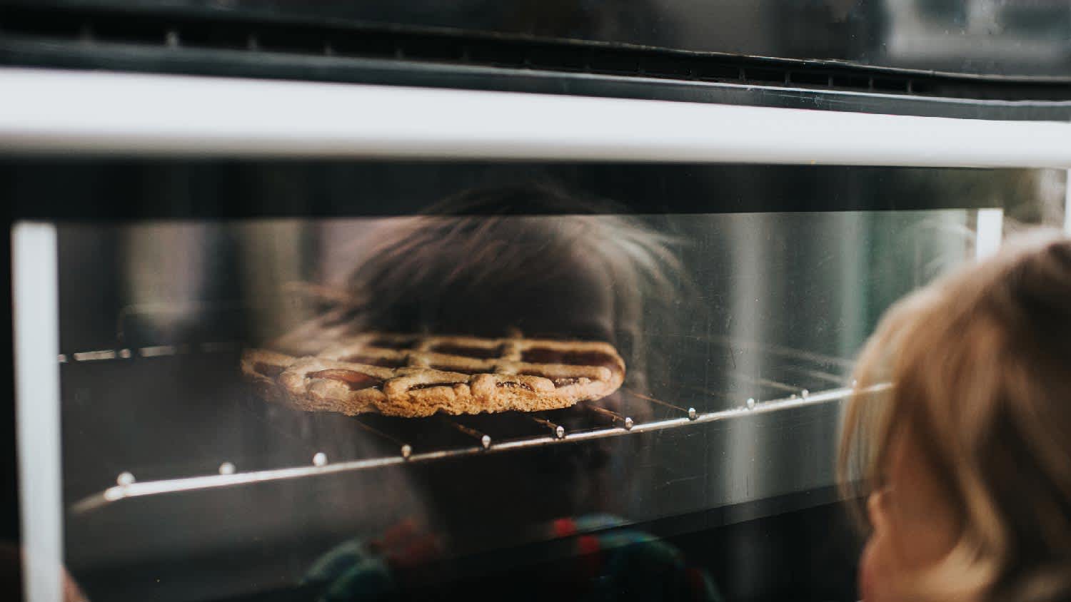 None A kid watching a pie in a steam oven