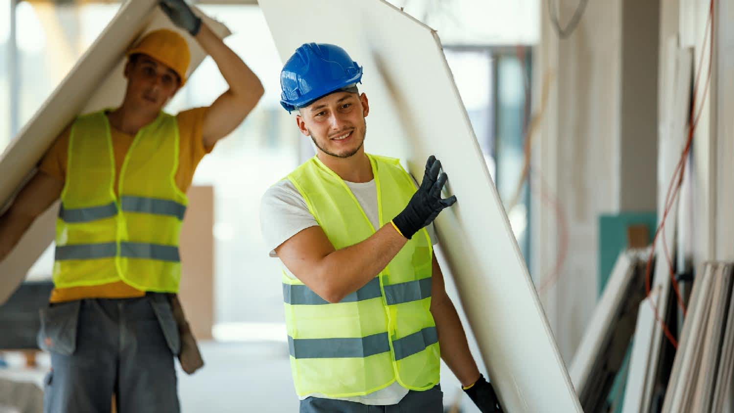 Two workers carrying pieces of drywall
