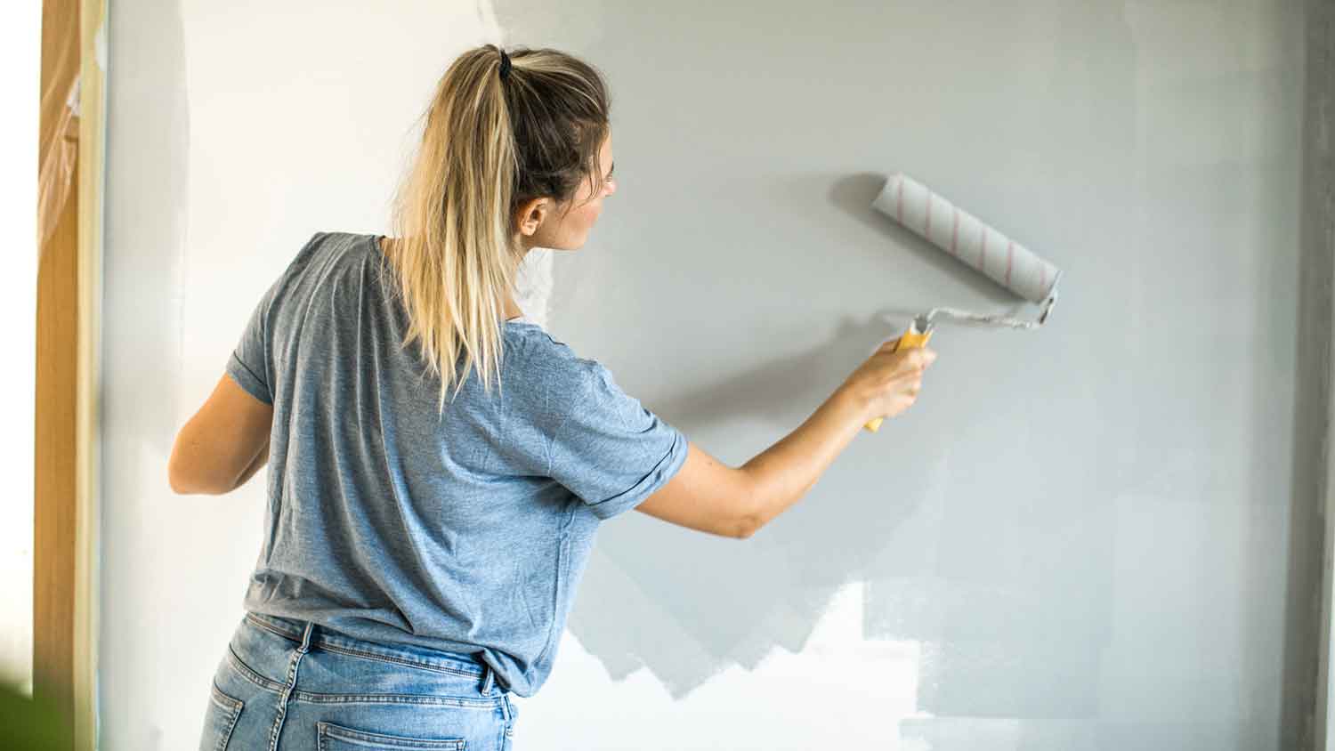 None Woman using a roller to paint an interior wall