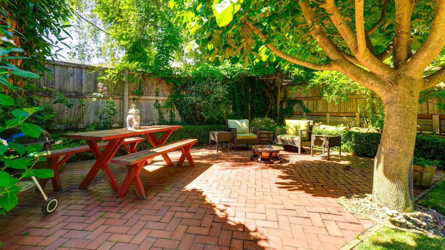 A cozy backyard brick patio with a large tree