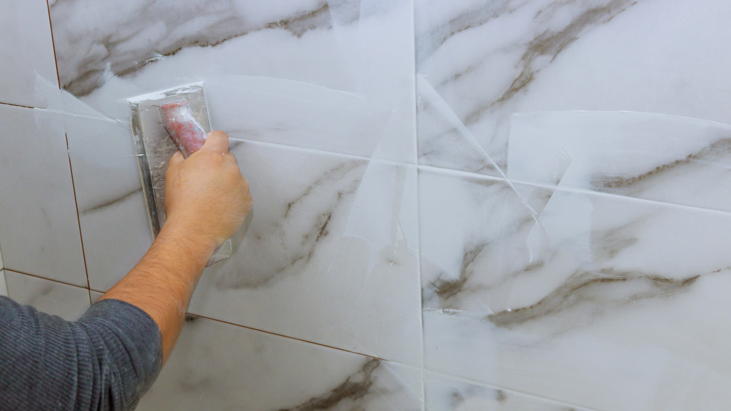None man smoothing out grout on marble tiles