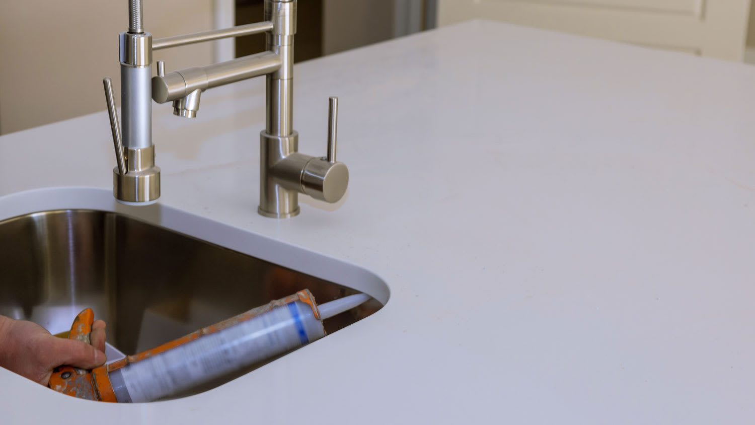 Close-up of a person applying silicone on an undermount sink