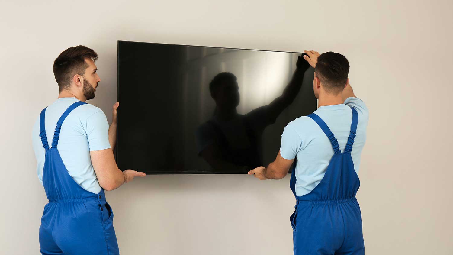 Couple of technicians lifting tv from wall mounting