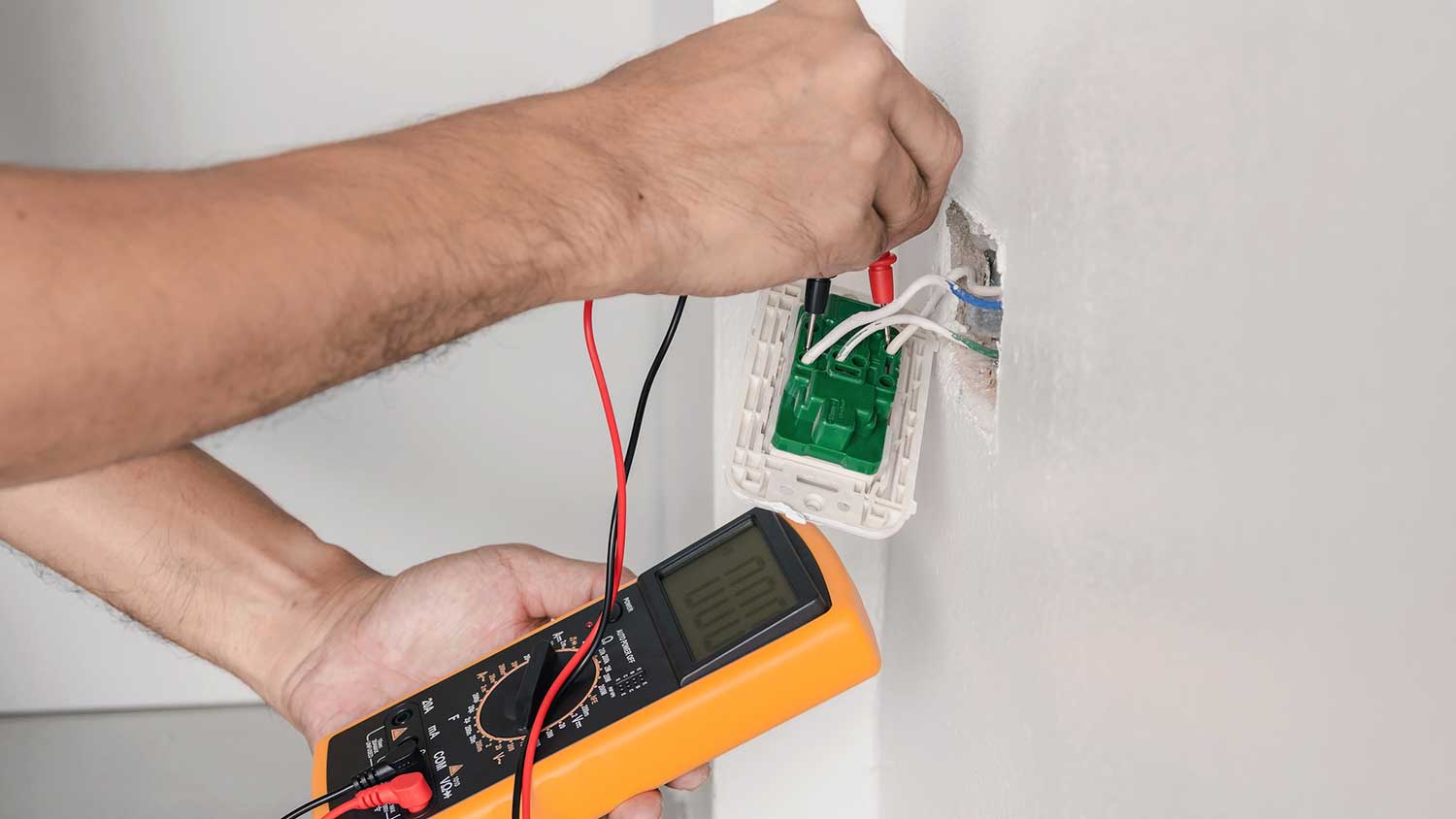 None Electrician using multimeter to identify wires in a wall outlet