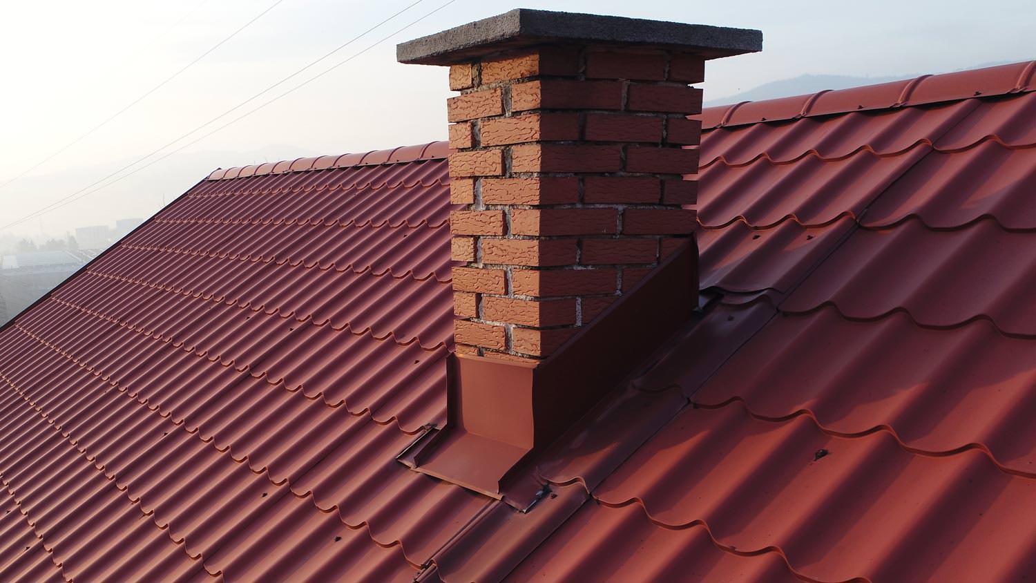 A metal roof of a house with a brick chimney