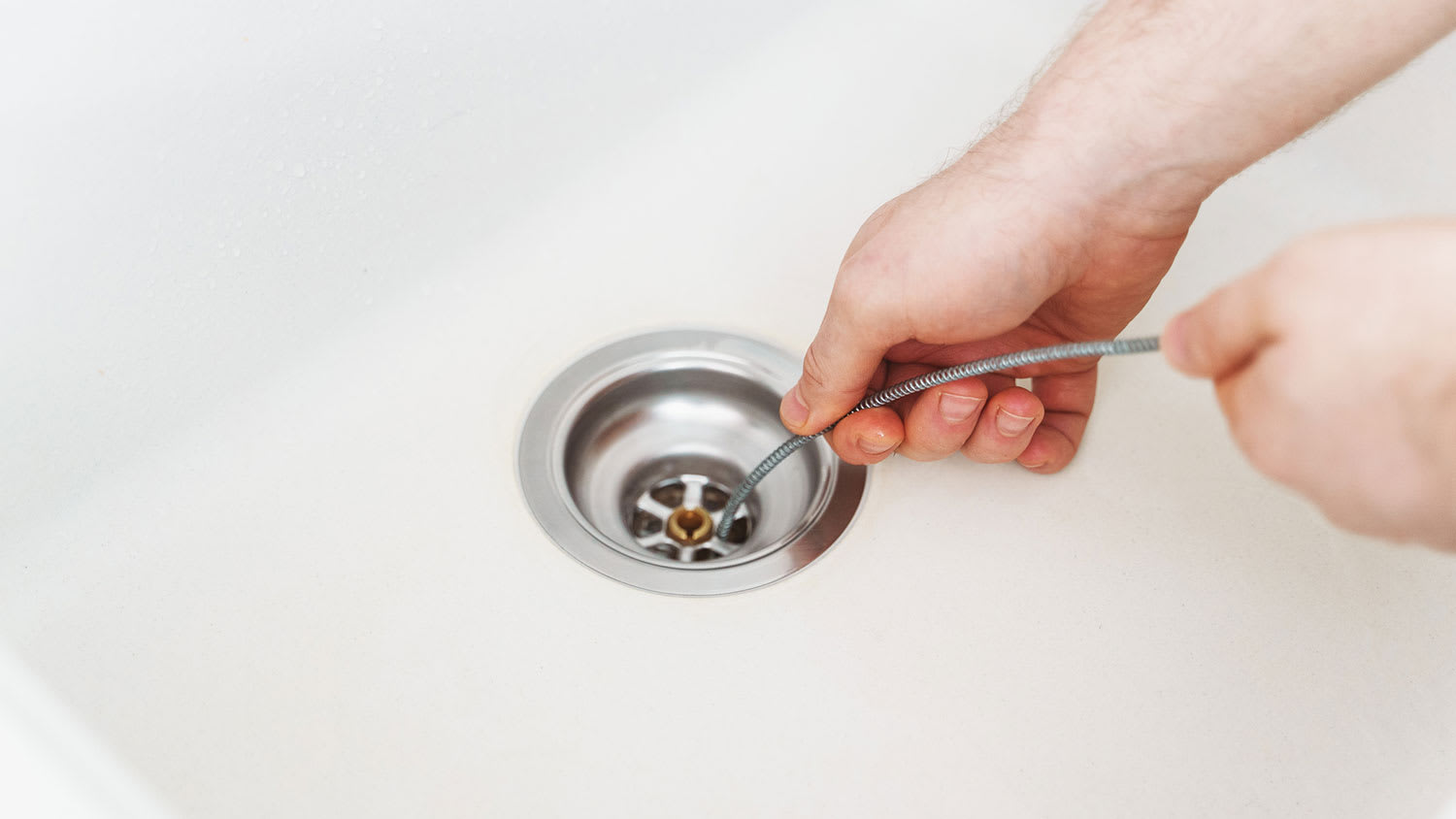 Plumber using drain snake to unclog kitchen sink