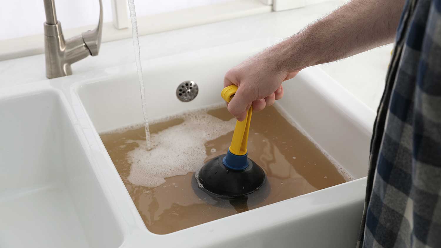 None man using plunger to unclog double kitchen sink