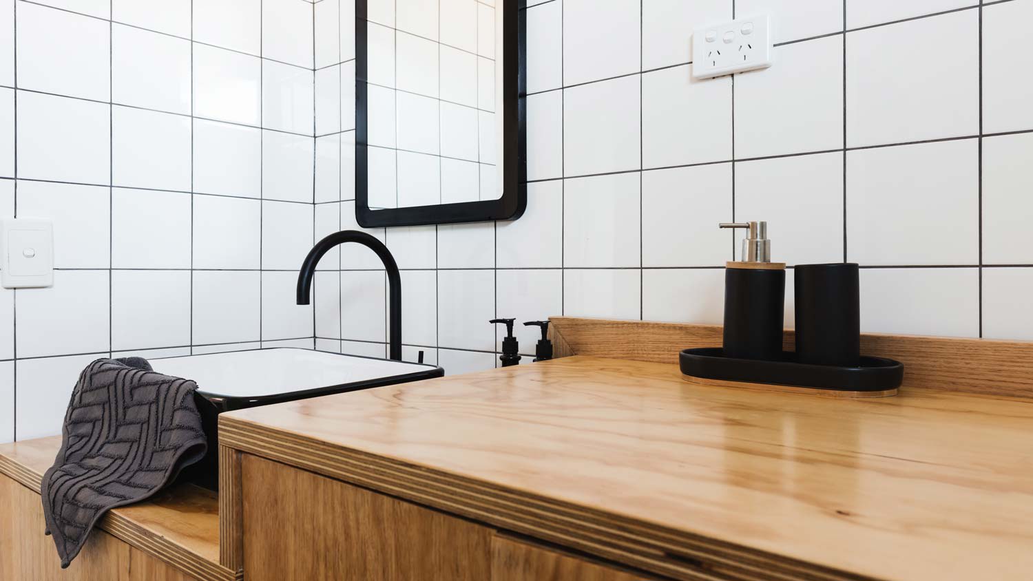 None A wooden vanity and a black basin in a small bathroom