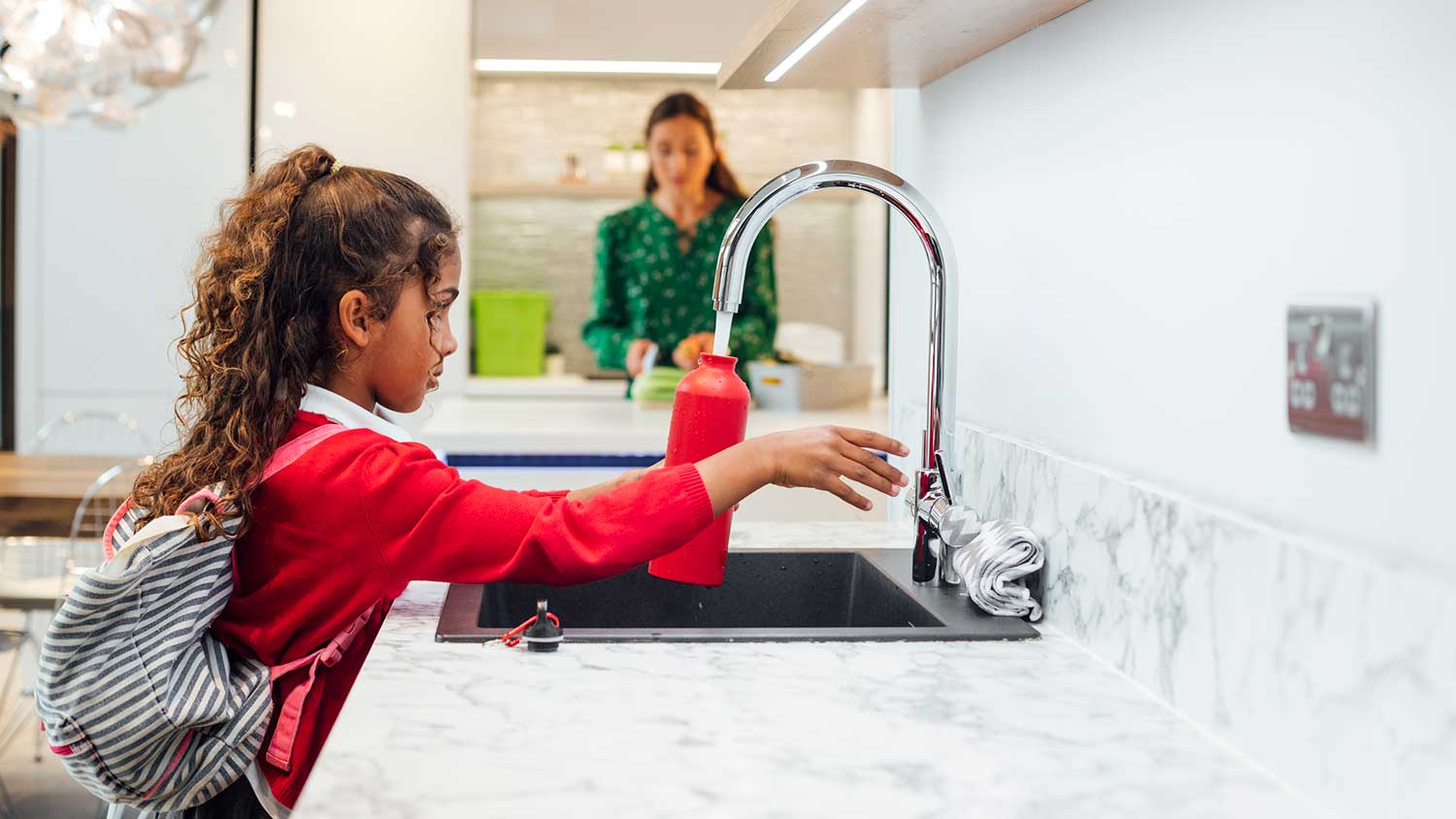 Girl using kitchen faucet to fill up a water bottle