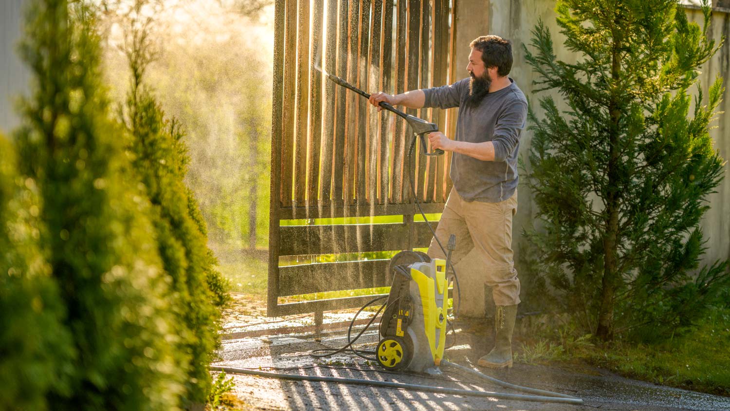A man cleaning a wooden gate using a pressure washer