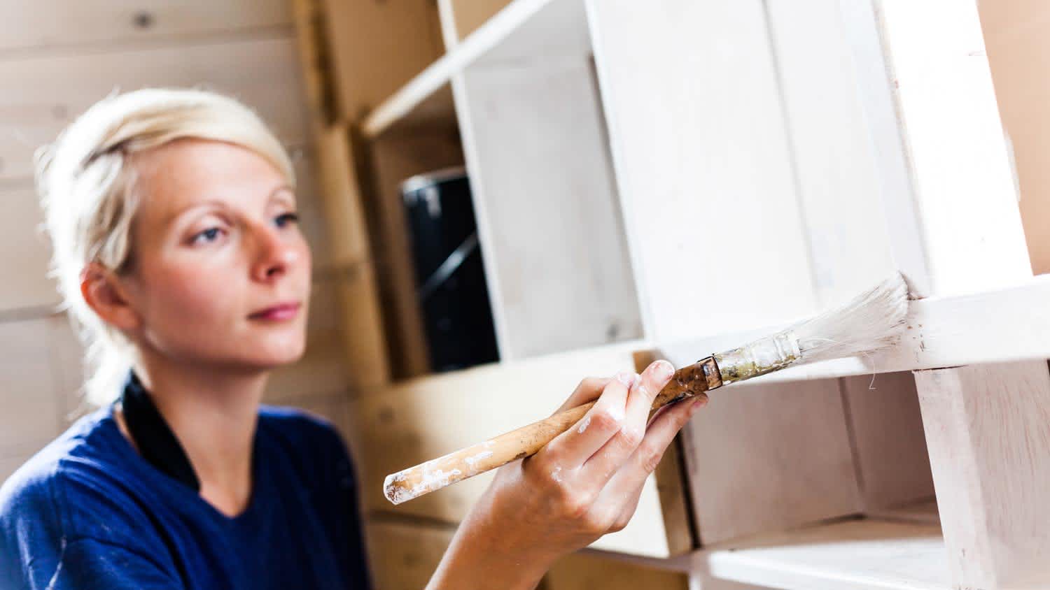 A woman painting kitchen furniture with a paint brush