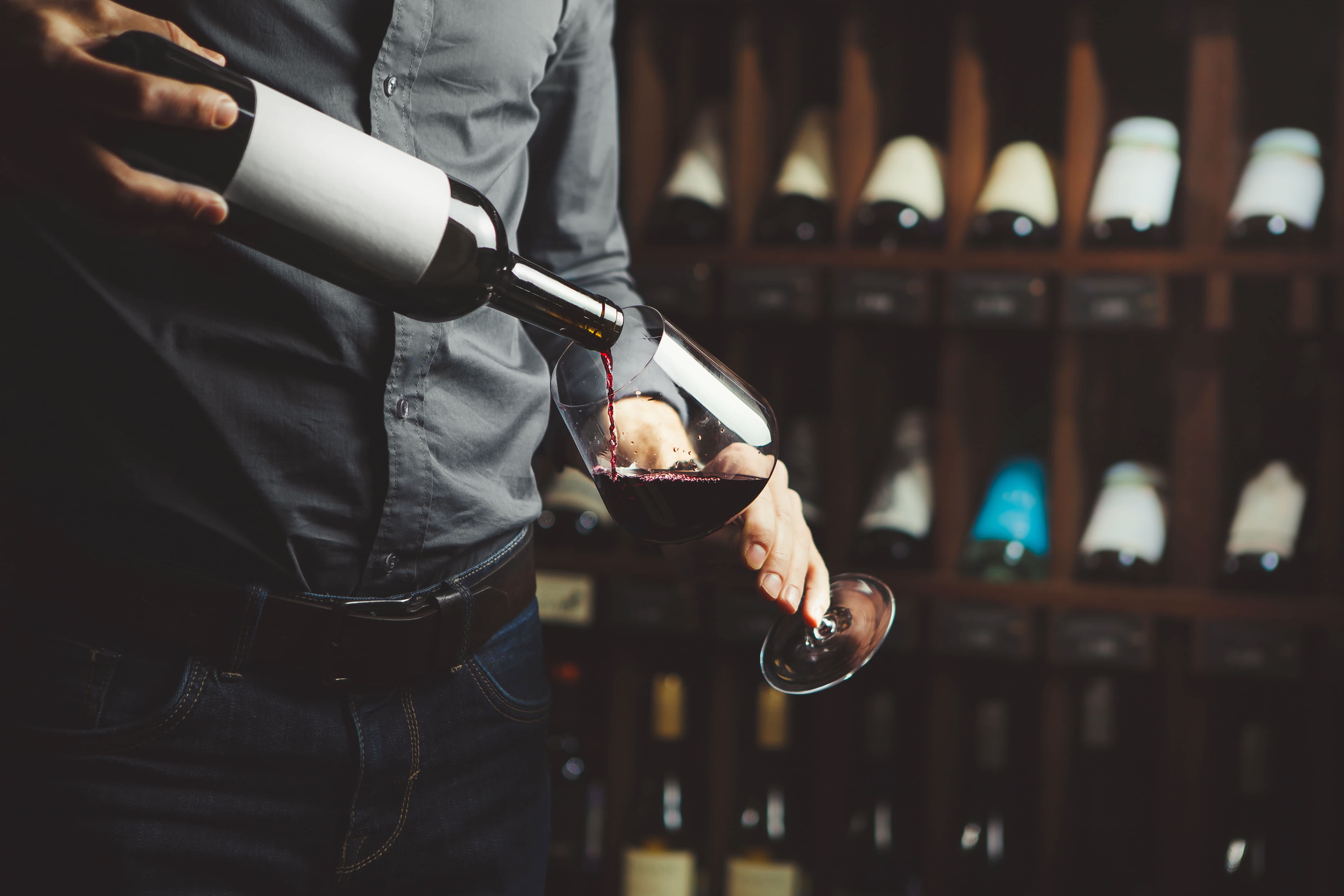 Man pouring glass of red wine in wine cellar
