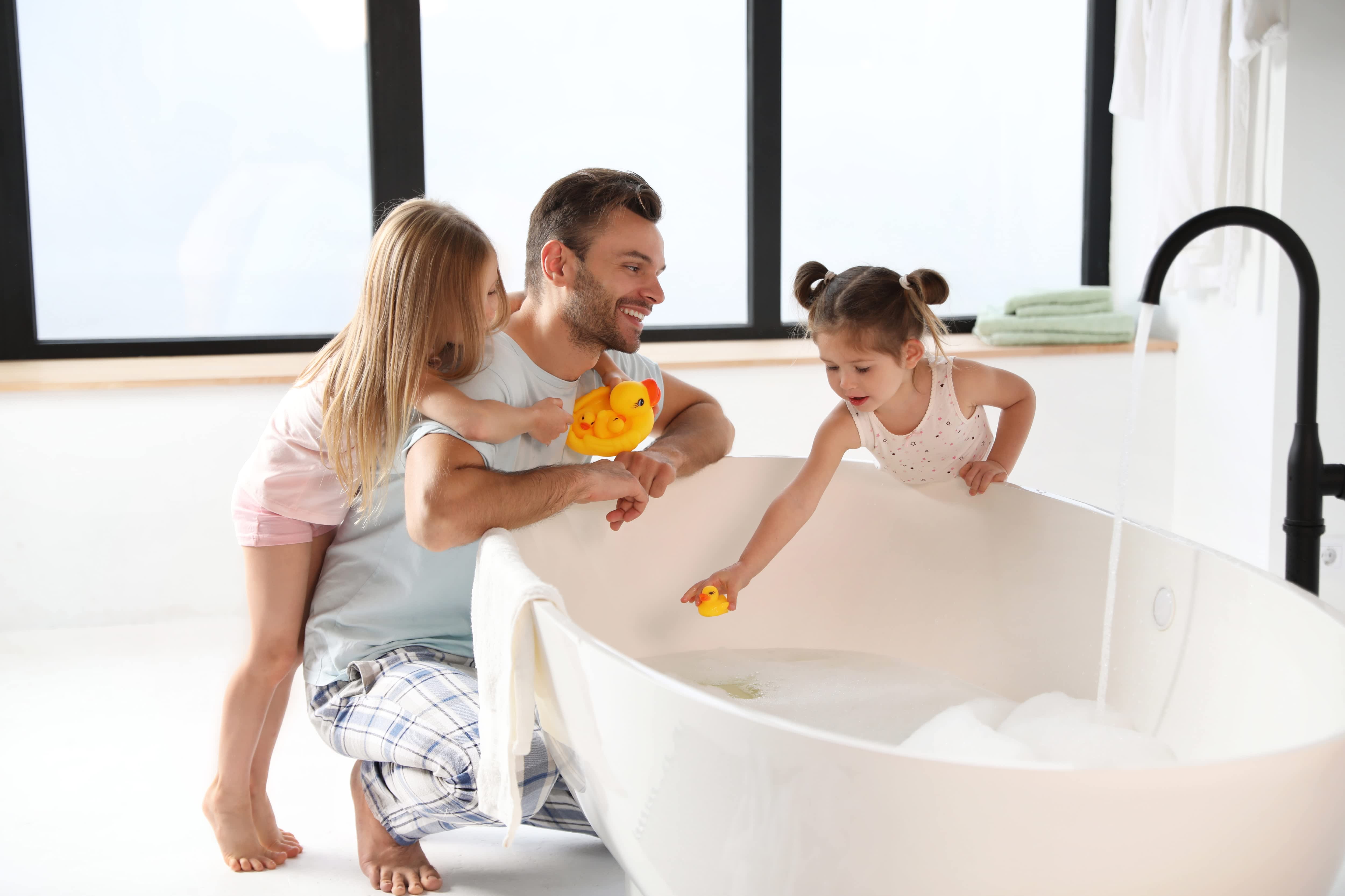 Young family playing in bathtub in modern bathroom