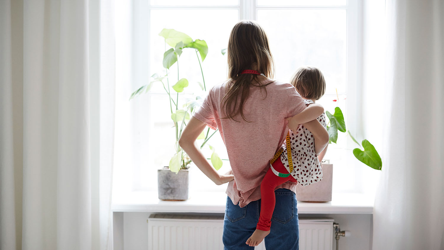 A woman and child stand in front of curtains with measuring tape