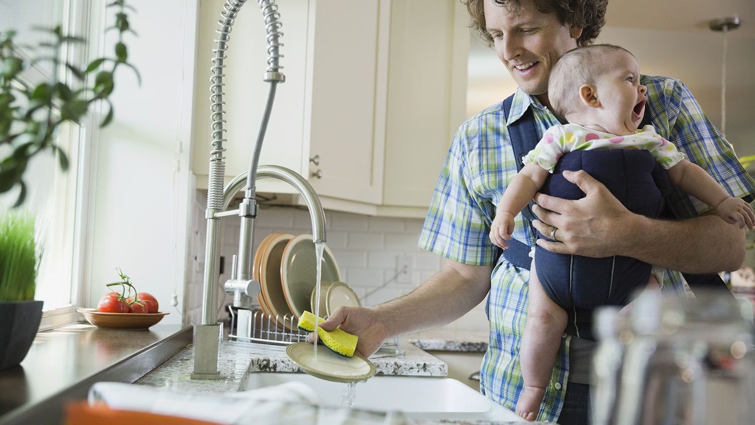 Father washing dishes while carrying baby girl