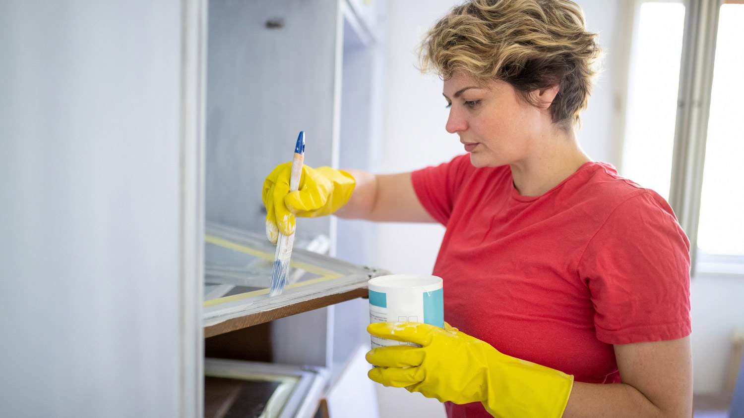 A woman using a brush painting a kitchen cabinet door