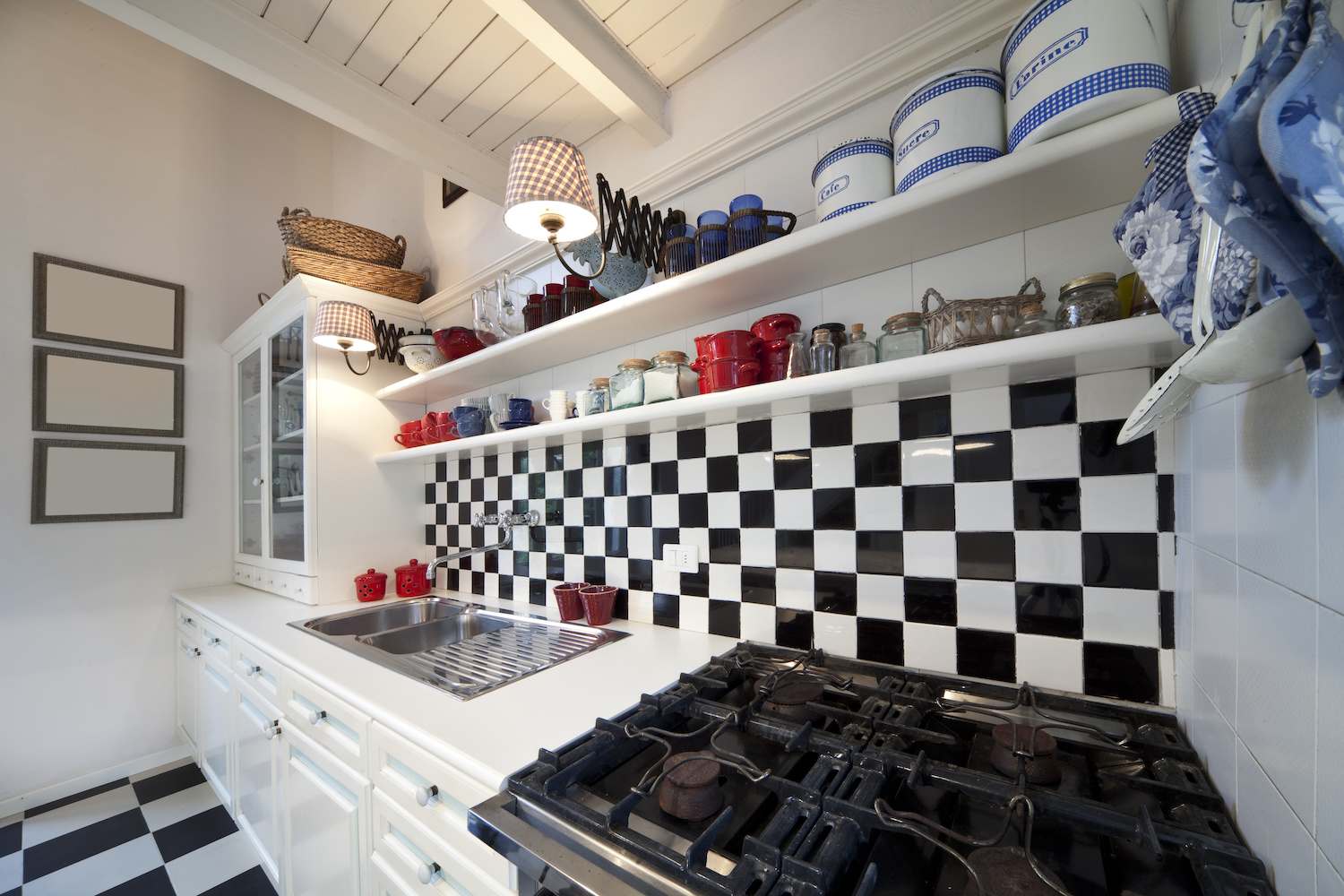 Kitchen with black-and-white checked tile backsplash, white cabinets, and retro tins on white open shelves