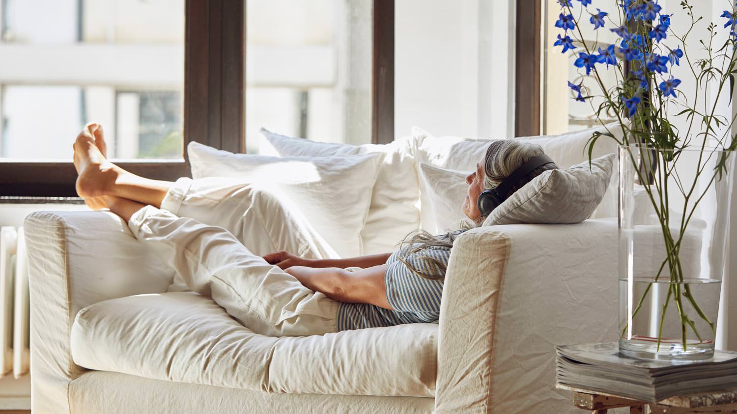 A senior woman lying on sofa listening to music in living room