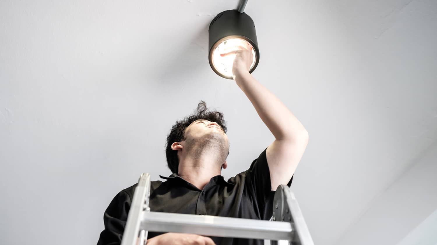 A man changing a light bulb while on a ladder