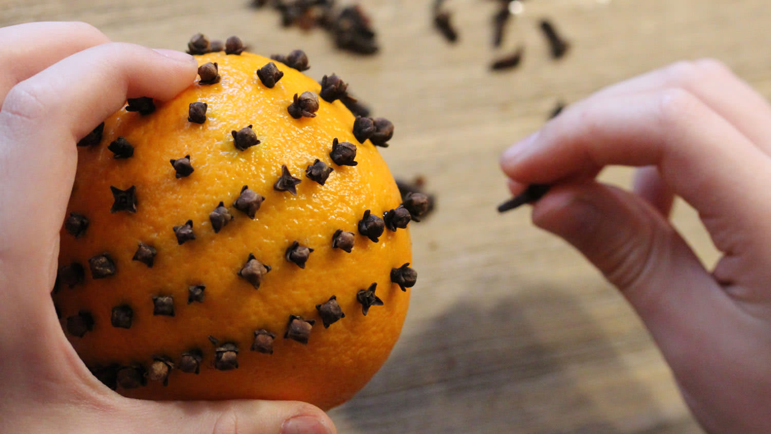 A woman’s hand putting cloves in an orange
