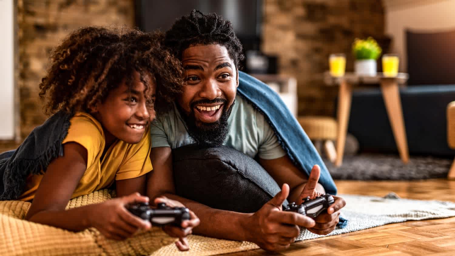 A father and a daughter covered in a blanket playing video games