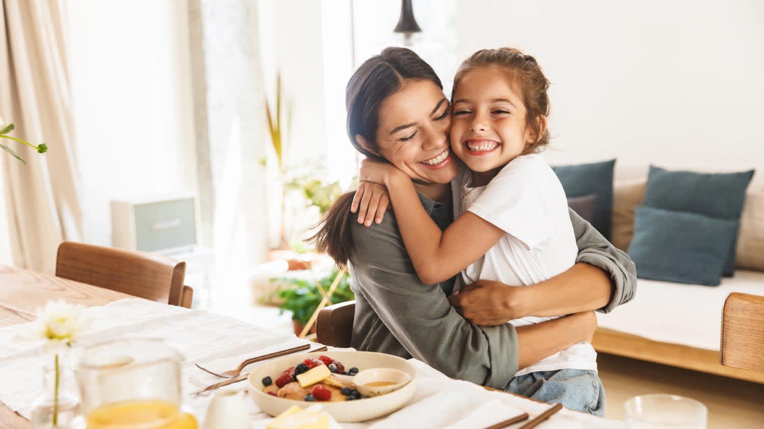 Mother and daughter hugging while having breakfast