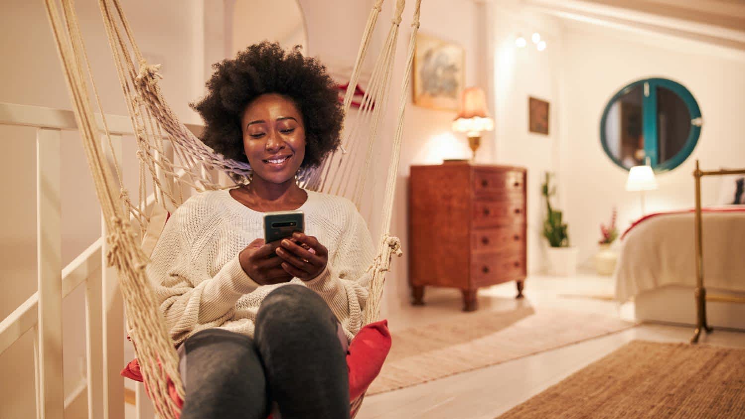 A woman using a mobile phone while sitting in a swing at home