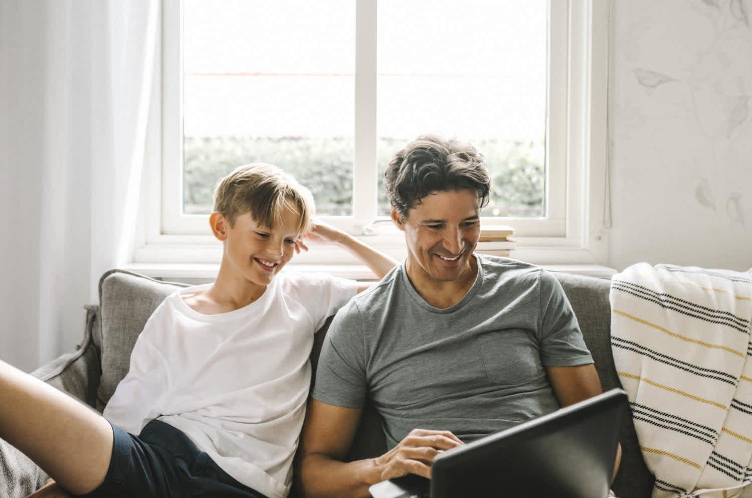 Father using laptop while sitting by son in living room