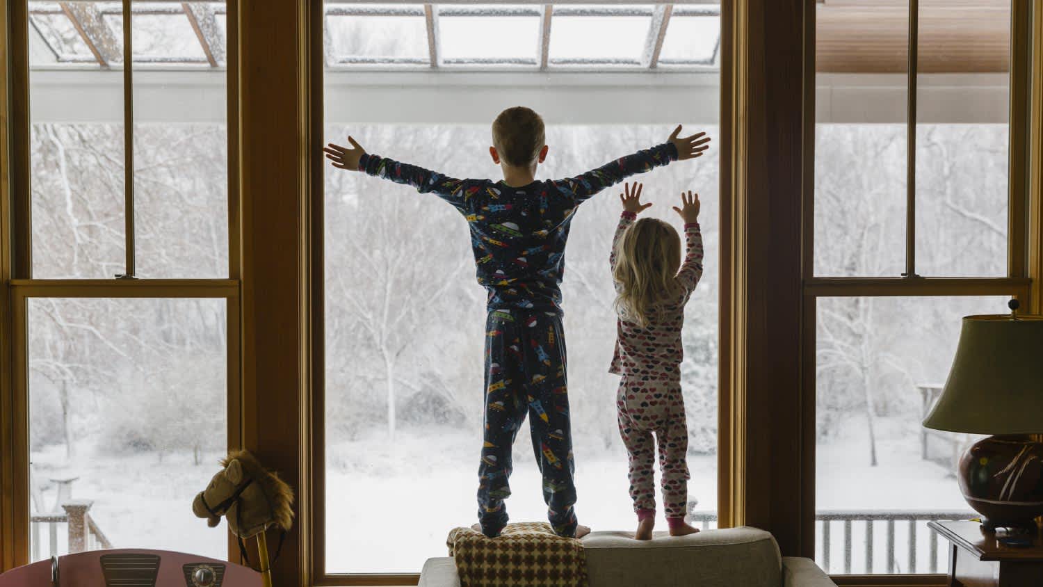 Brother and sister looking out window after snowstorm