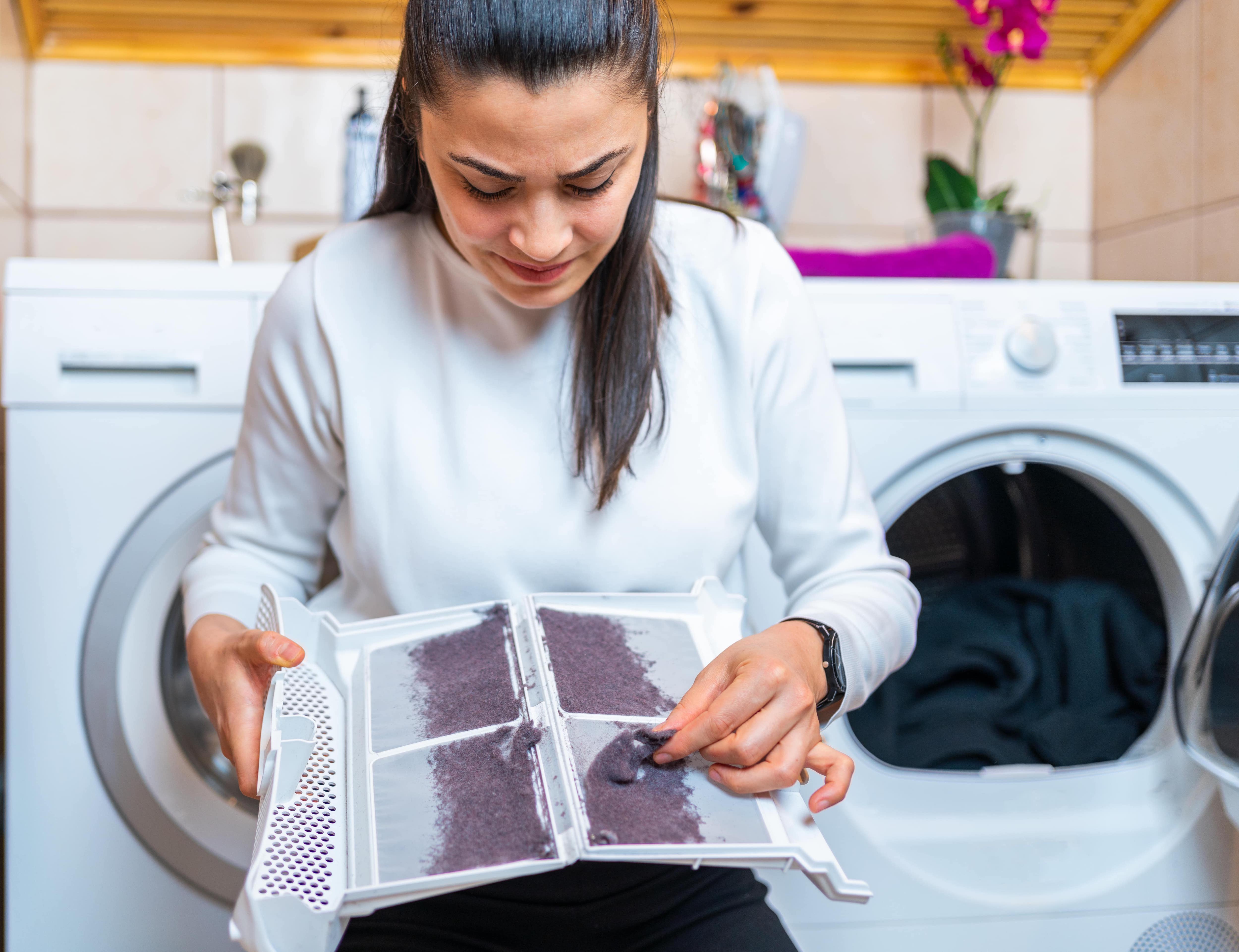 A young woman removing lint and dust from lint trap of a tumble dryer