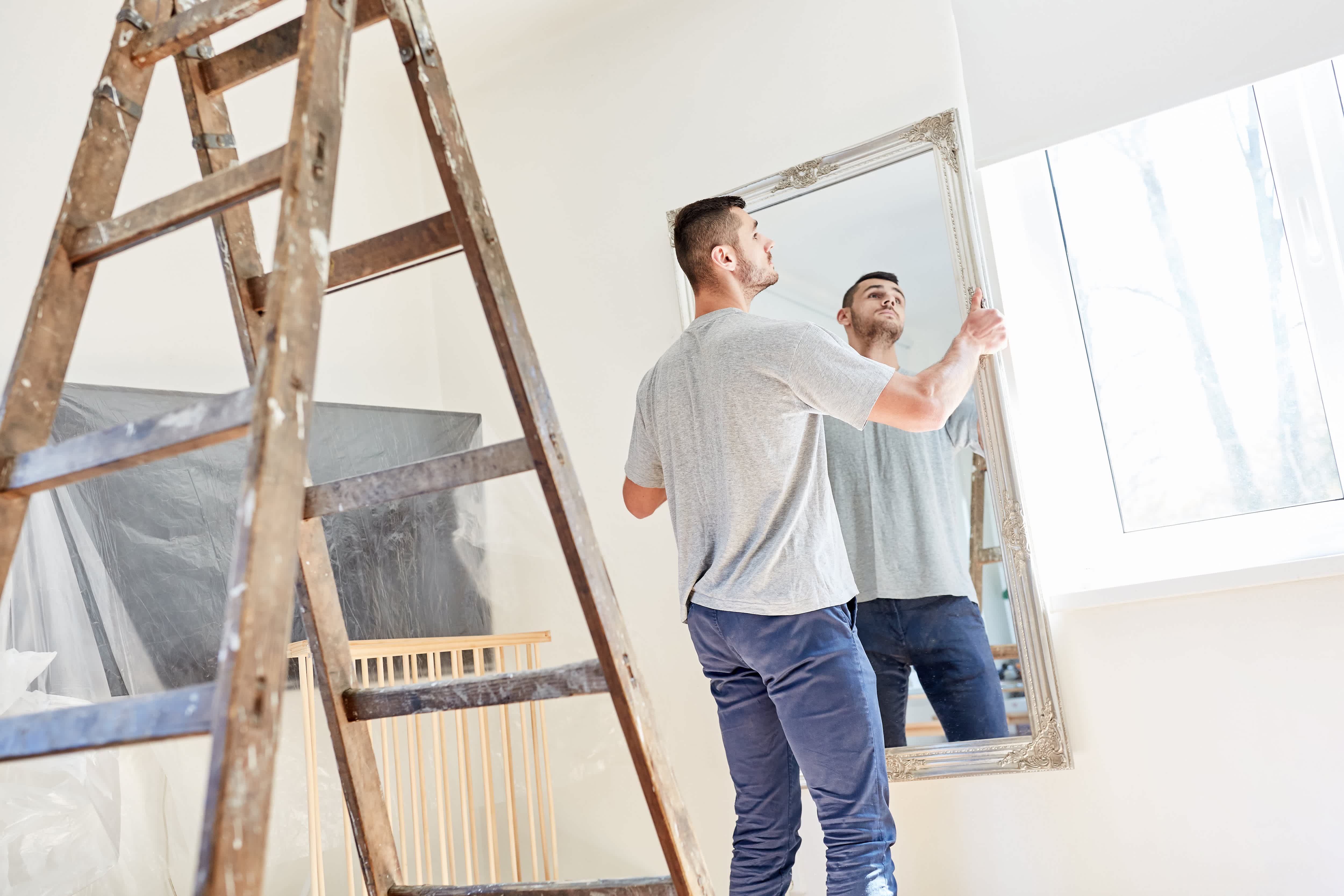 Man hanging large mirror in room