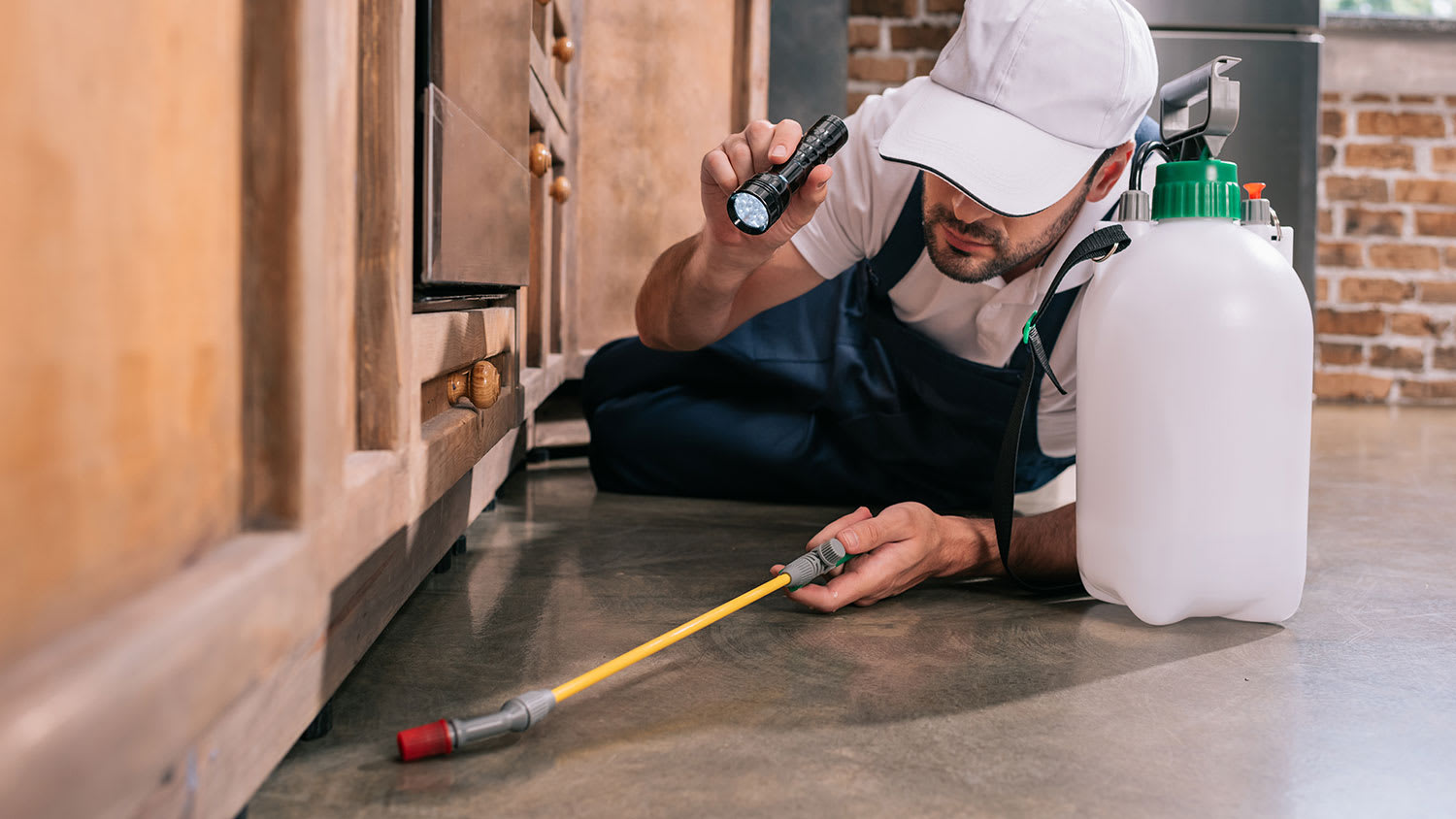 Pest control worker lying on floor spraying pesticide