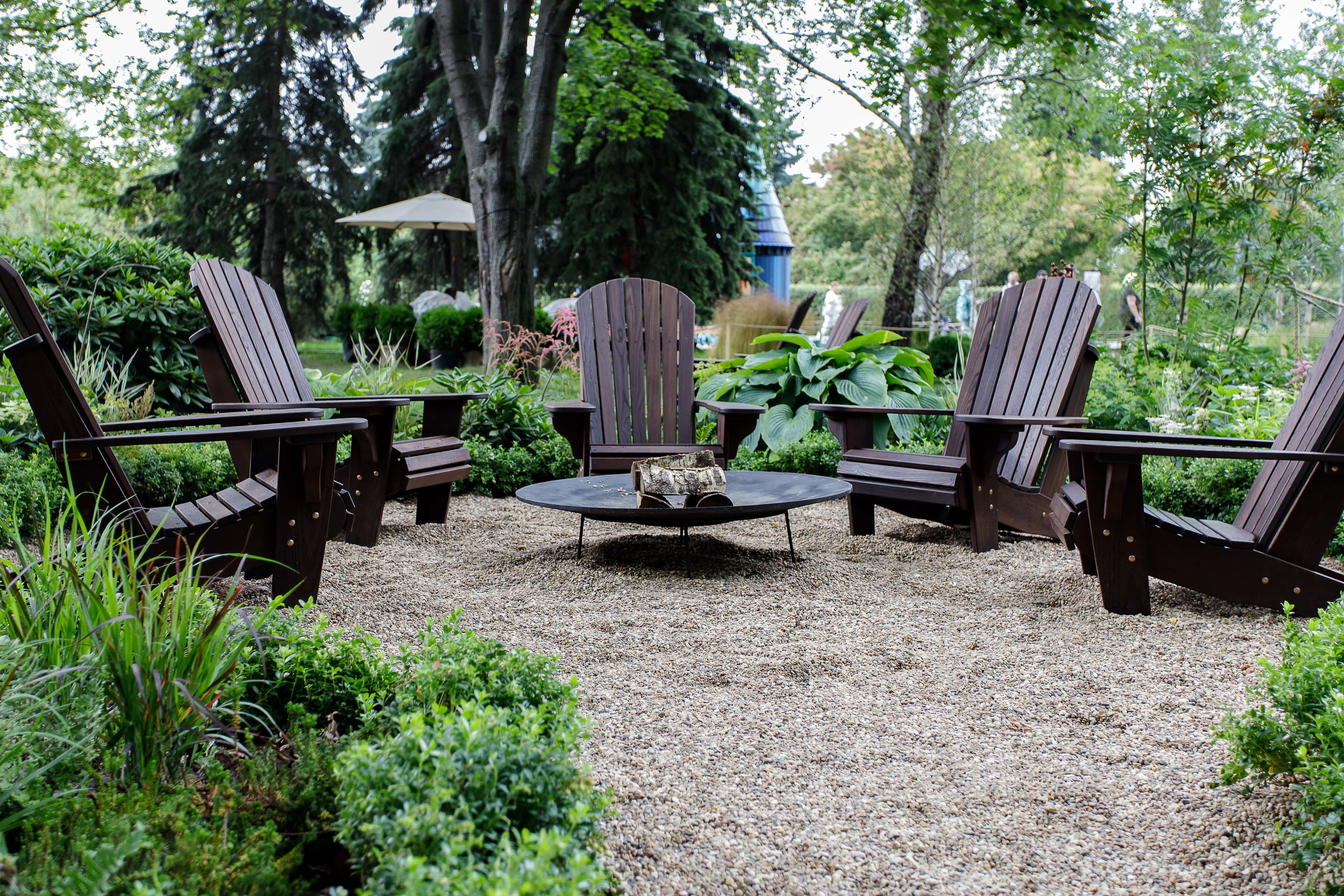 A metal fire pit surrounded by Adirondack chairs on a gravel bed