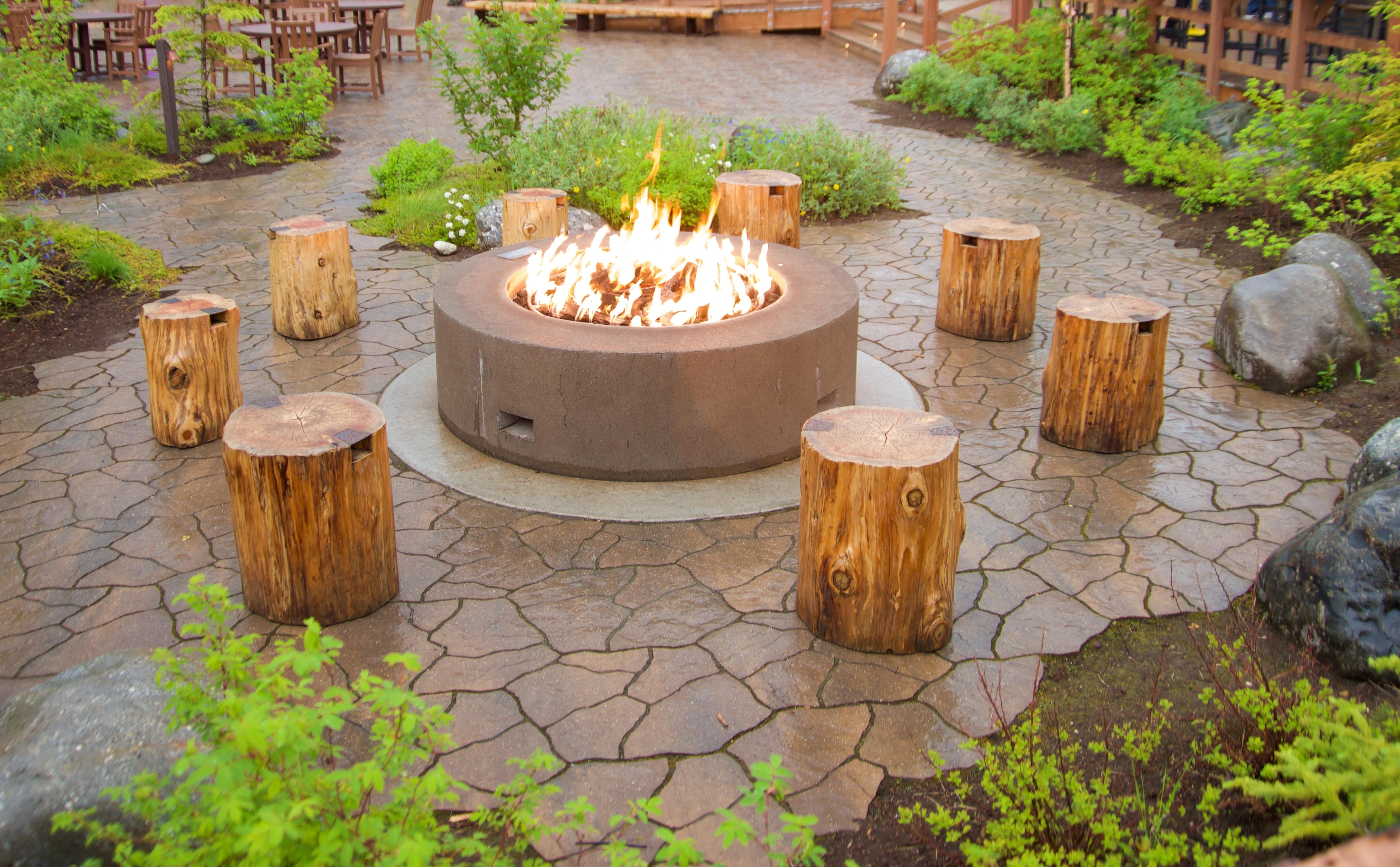 A round, cement fire pit surrounded by tree stump seating