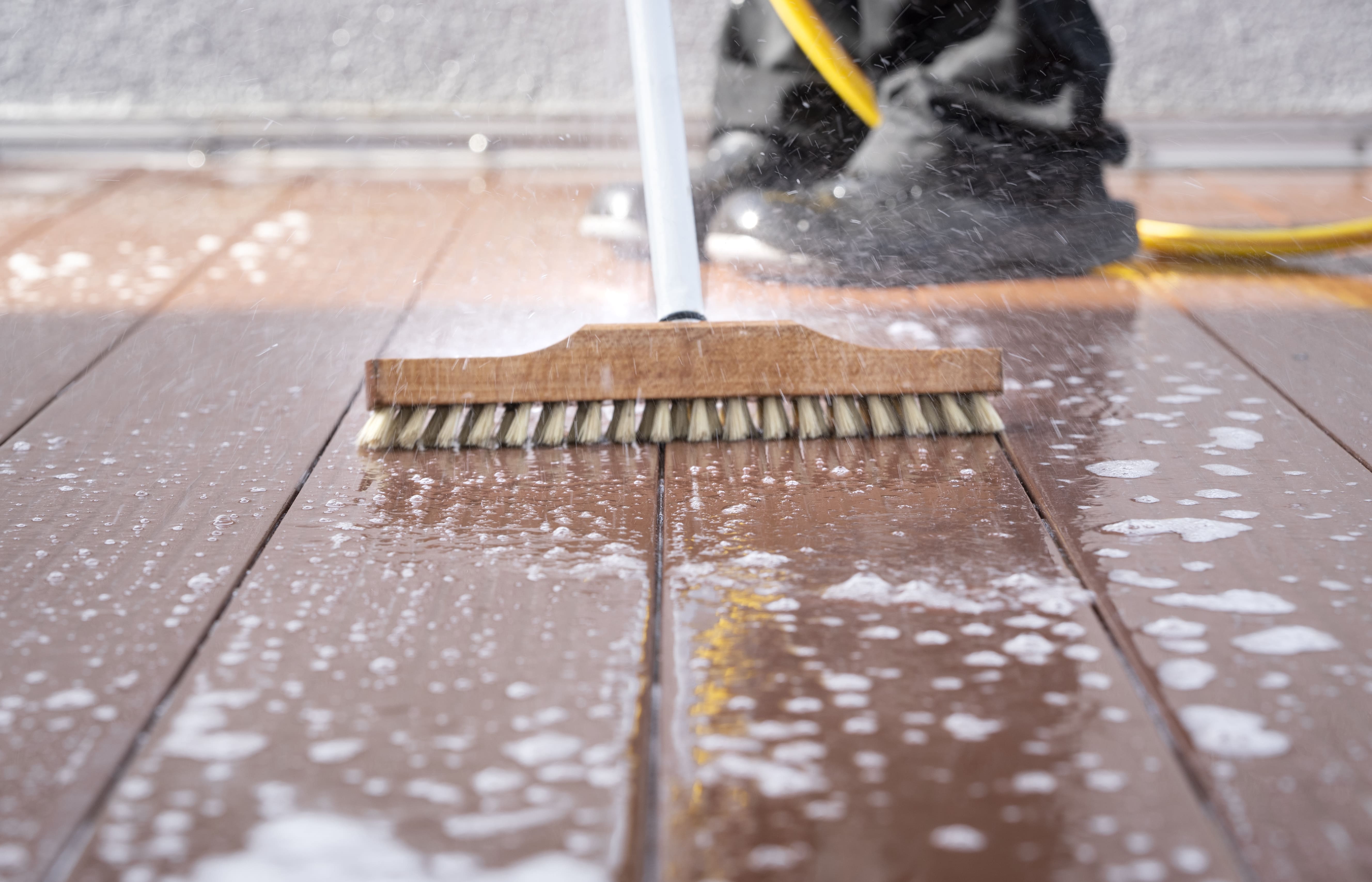 A person in black pants and shoes scrubbing a deck with a bristle brush