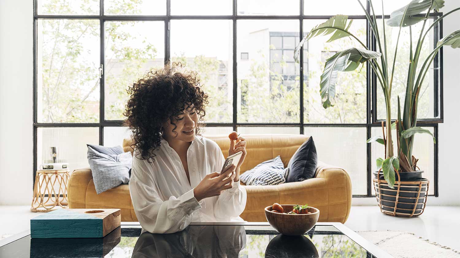 woman holding her phone and eating a strawberry