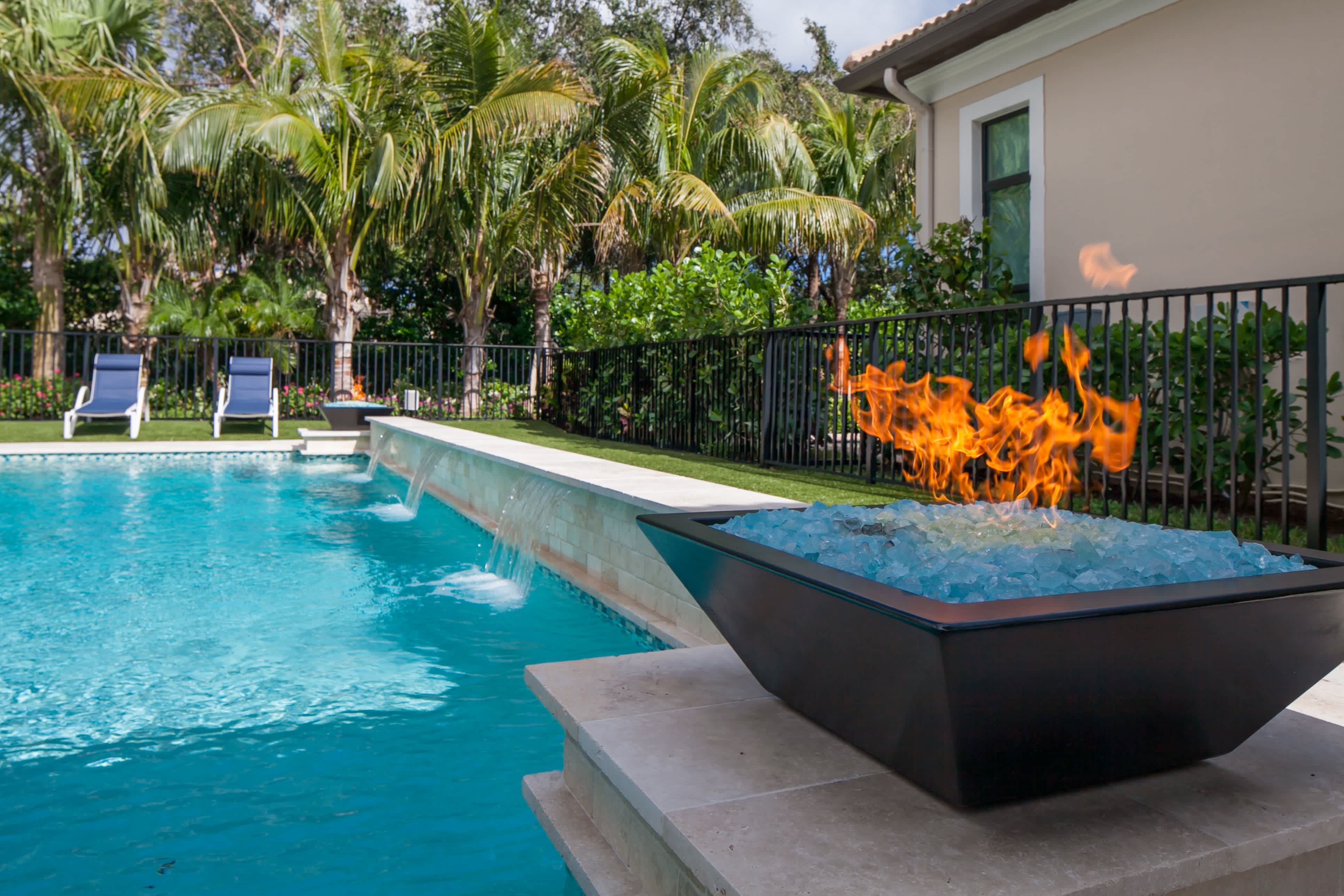 A gas fire pit with glass stones next to an inground pool