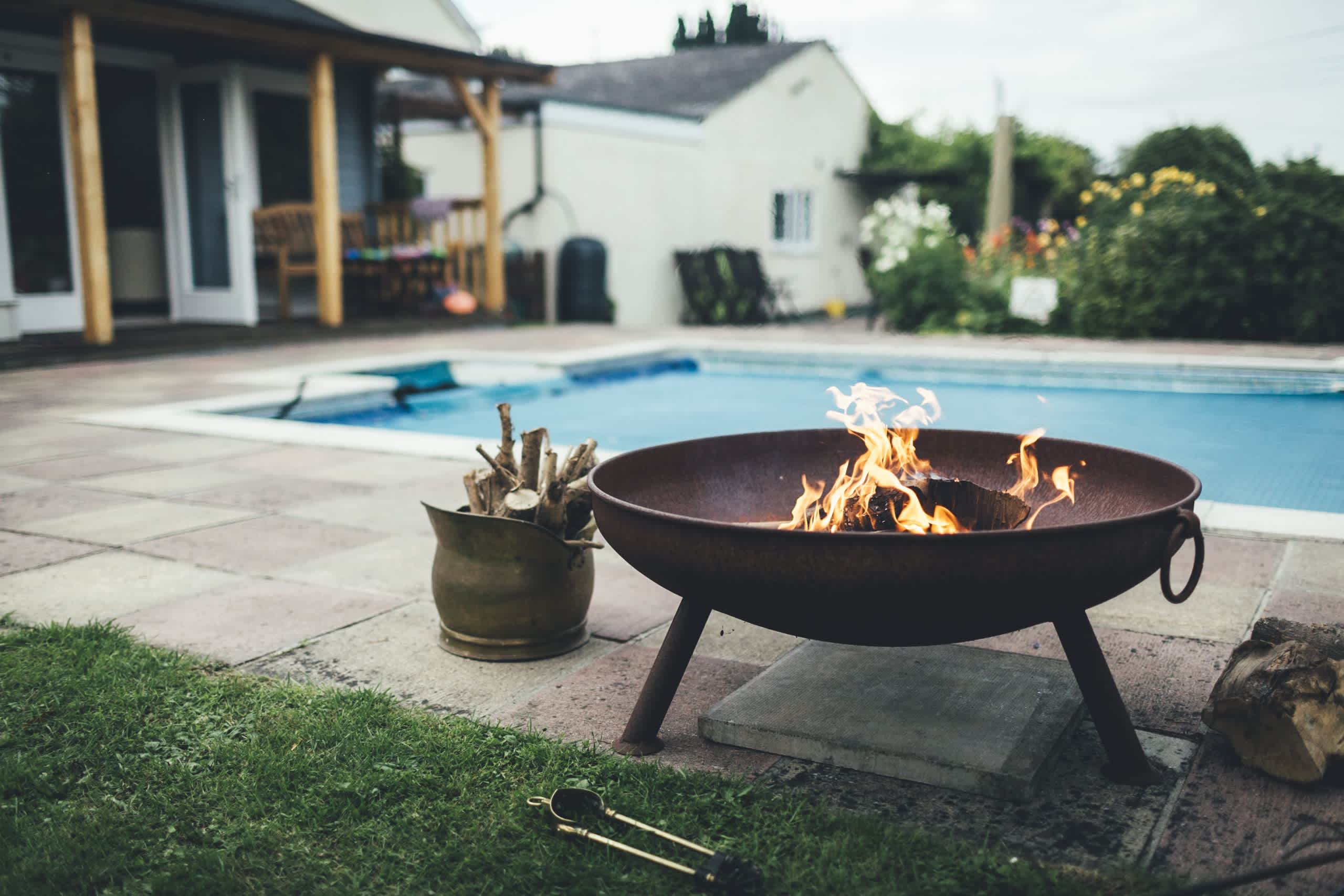 A metal bowl fire pit with three legs next to an inground pool