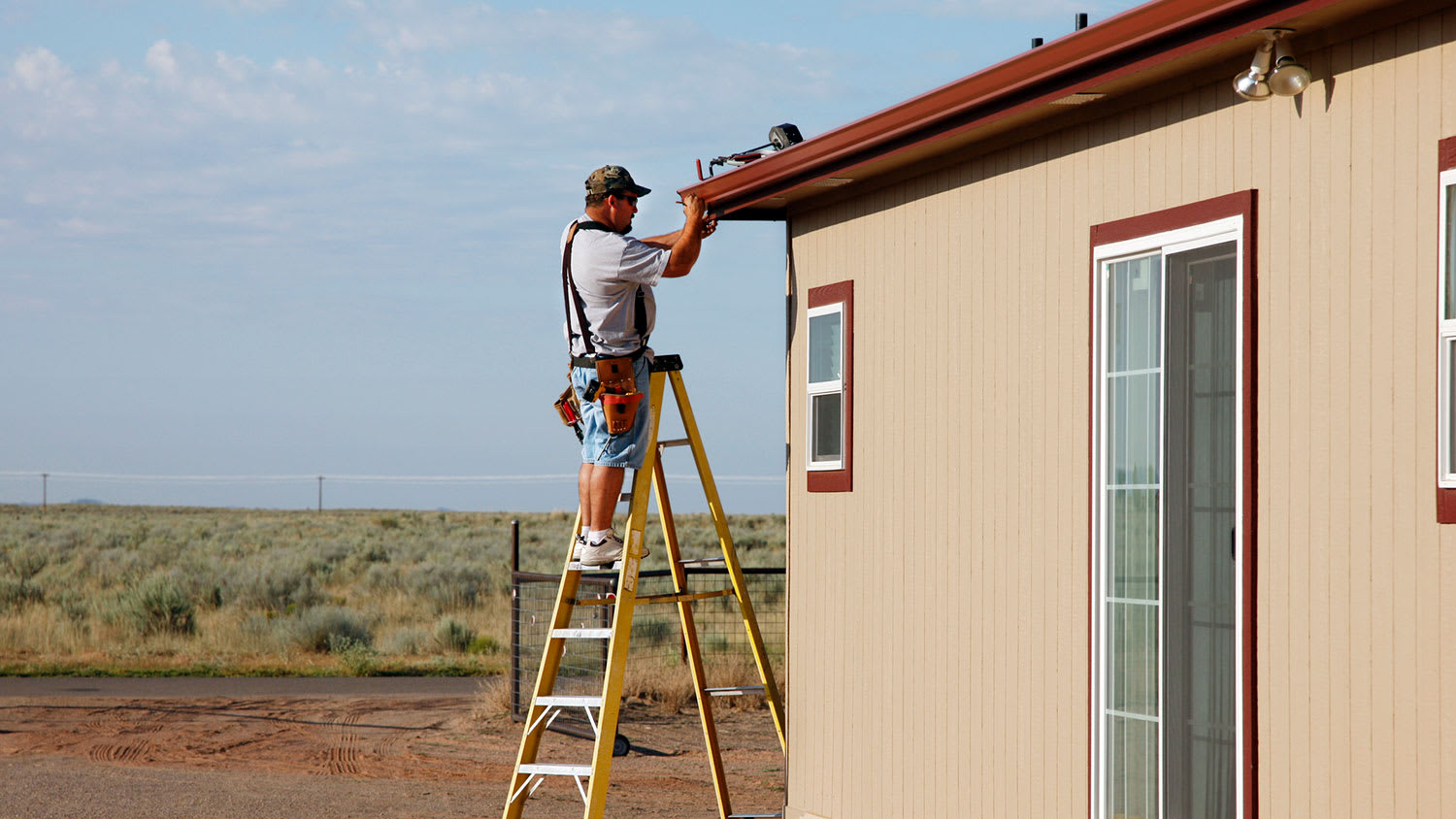 Handyman on a yellow ladder installing house gutters