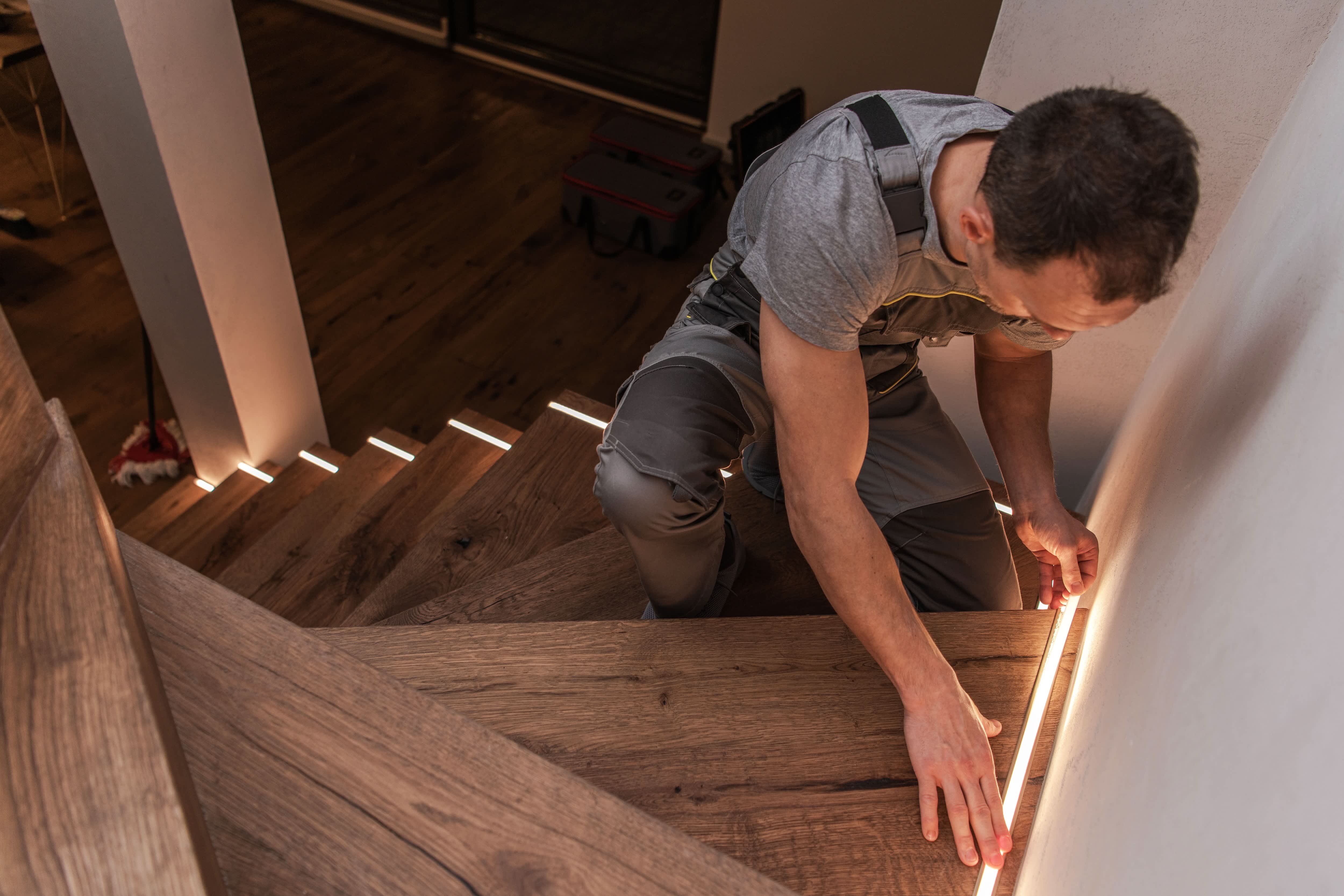 man installing LED light strips to a wooden interior staircase