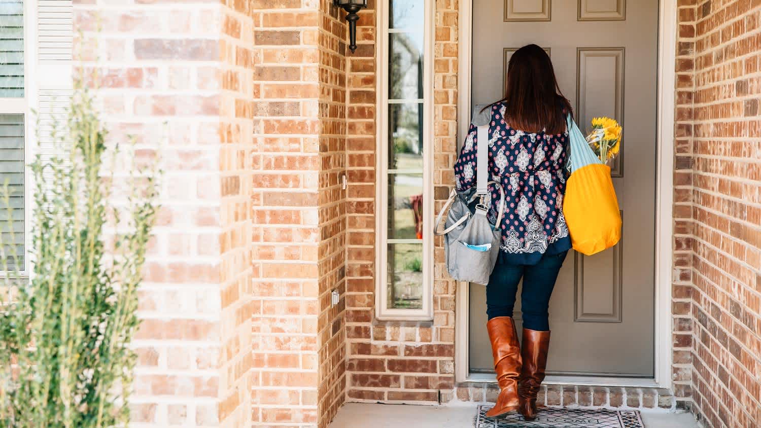 A woman holding flowers entering a brick house