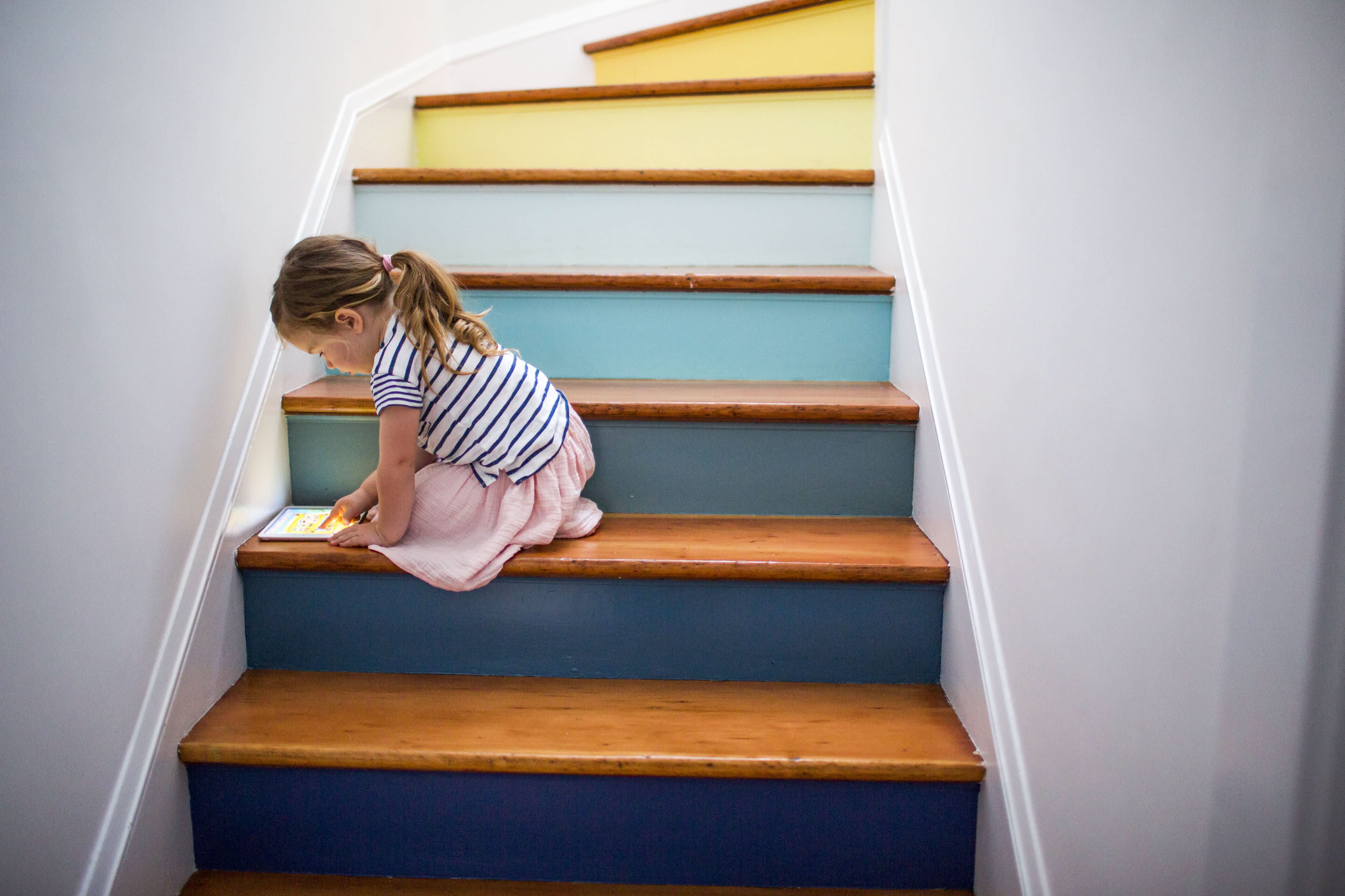 A young girl playing on a tablet while sitting on an interior staircase