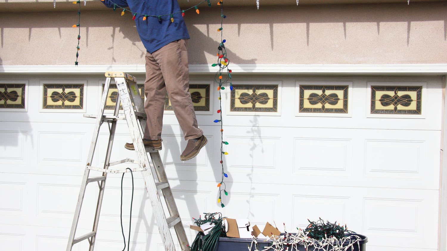 A man on a ladder hanging Christmas lights above the garage door