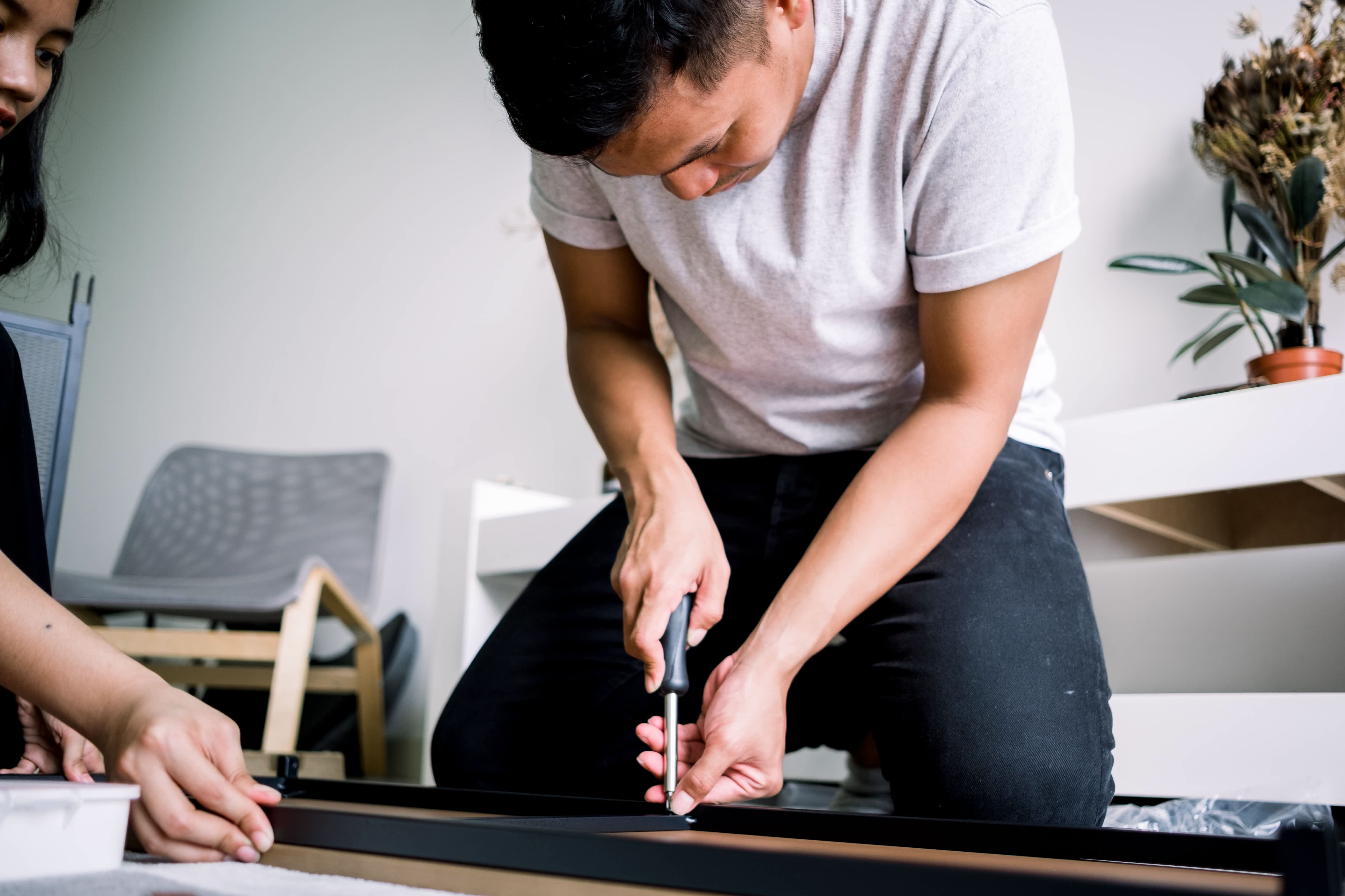 A young man using a screwdriver to assemble a table