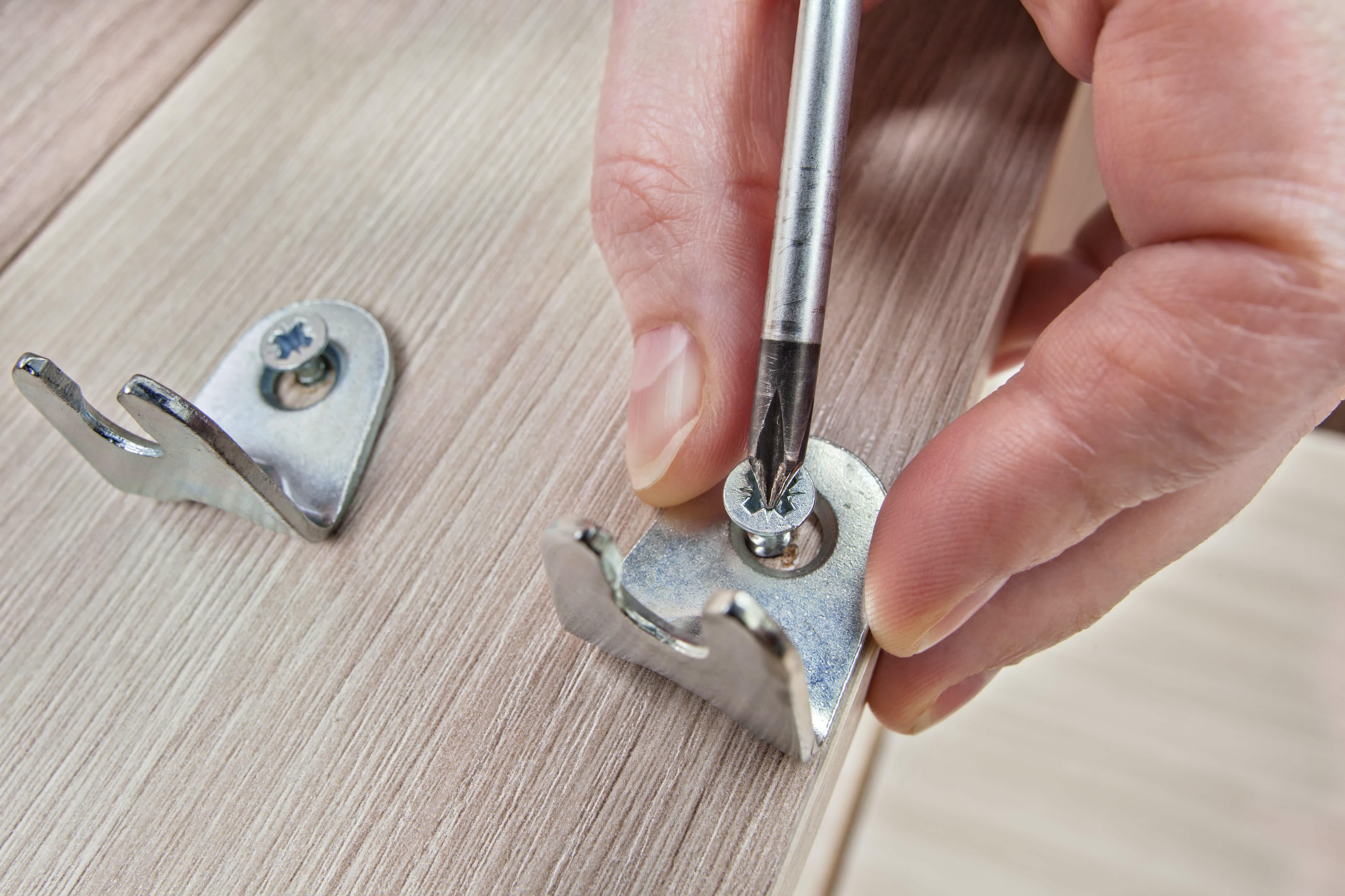 A close up of a person using a screwdriver to secure a bracket into wood